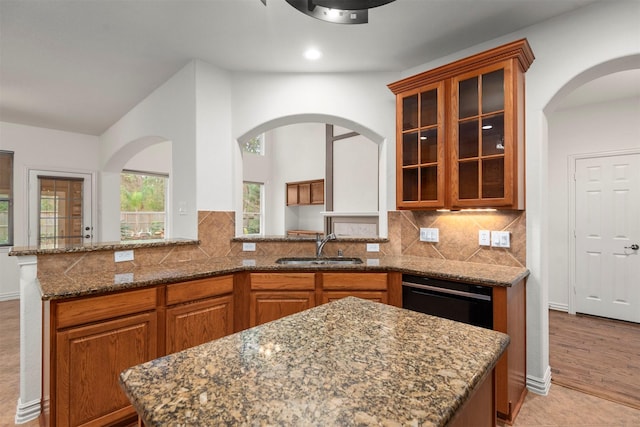 kitchen with backsplash, light stone countertops, kitchen peninsula, and sink