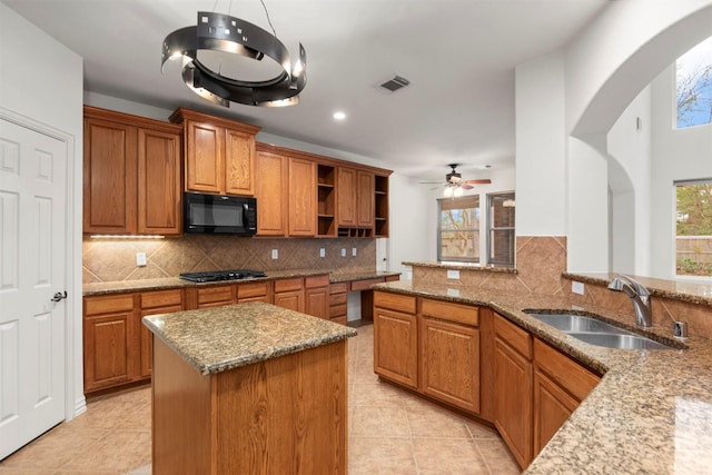 kitchen featuring decorative backsplash, light stone counters, ceiling fan, and sink