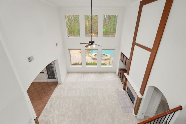 living room with ceiling fan, a towering ceiling, a fireplace, and ornamental molding