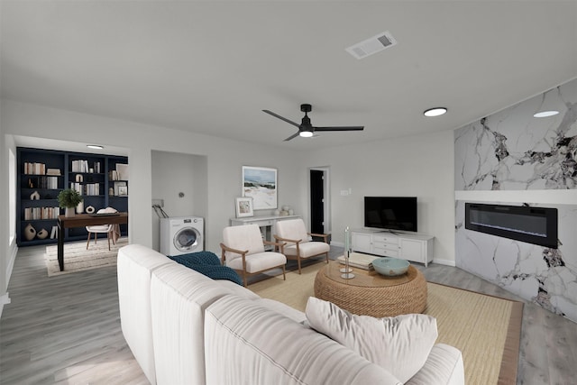 living room with washer / clothes dryer, a premium fireplace, light hardwood / wood-style flooring, and ceiling fan