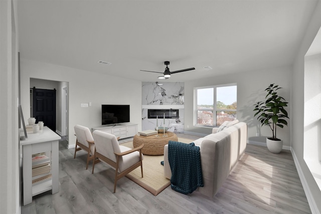 living room featuring a high end fireplace, a barn door, light hardwood / wood-style floors, and ceiling fan