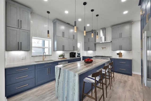 kitchen with sink, wall chimney exhaust hood, light wood-type flooring, decorative light fixtures, and a kitchen island