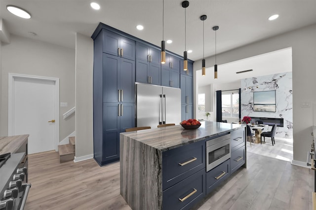 kitchen with a center island, blue cabinets, built in appliances, dark stone countertops, and decorative light fixtures