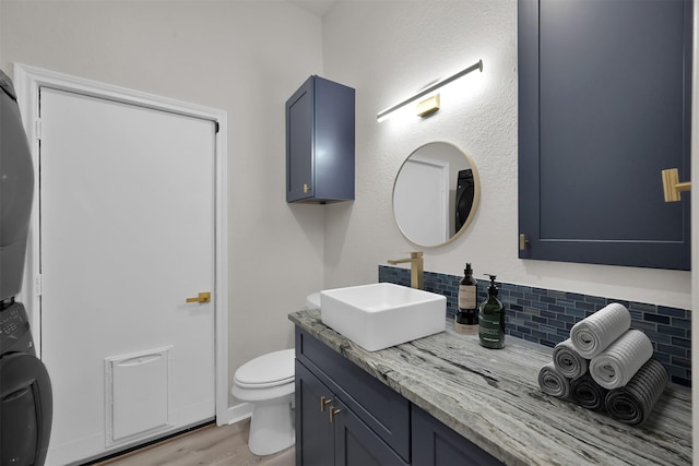 bathroom featuring decorative backsplash, vanity, hardwood / wood-style flooring, toilet, and stacked washer / drying machine