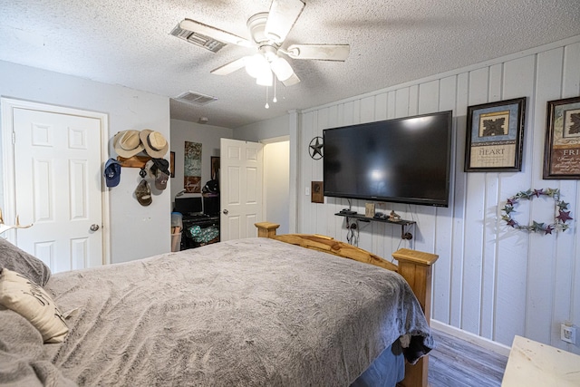 bedroom featuring ceiling fan, wooden walls, a textured ceiling, and hardwood / wood-style flooring