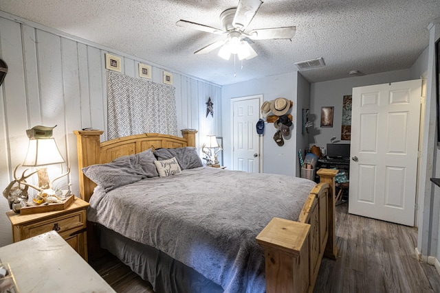 bedroom with a textured ceiling, ceiling fan, dark wood-type flooring, and wood walls