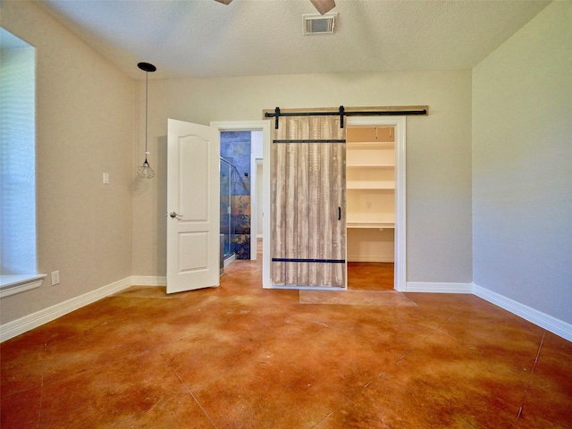 unfurnished bedroom featuring a walk in closet, ceiling fan, a barn door, a textured ceiling, and a closet