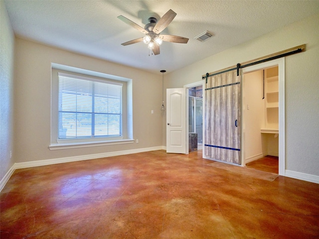 unfurnished bedroom with ceiling fan, a barn door, a textured ceiling, and a closet