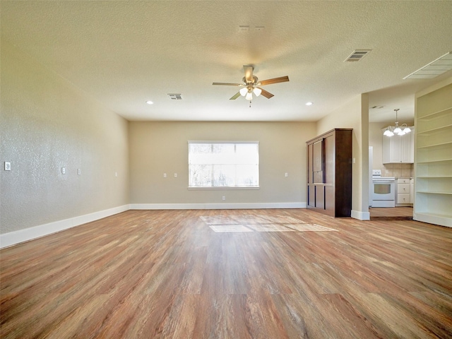 unfurnished living room featuring ceiling fan with notable chandelier, light wood-type flooring, and a textured ceiling