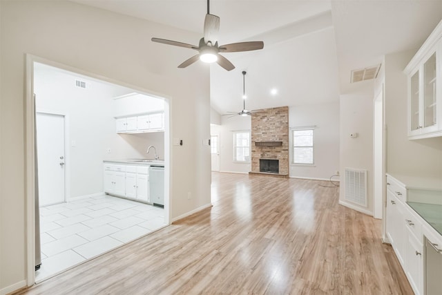 unfurnished living room featuring ceiling fan, sink, high vaulted ceiling, light hardwood / wood-style flooring, and a stone fireplace