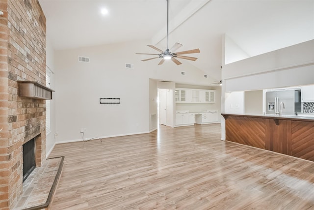 unfurnished living room featuring ceiling fan, high vaulted ceiling, light hardwood / wood-style flooring, beamed ceiling, and a fireplace