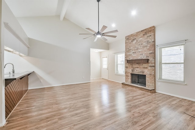 unfurnished living room with a wealth of natural light, ceiling fan, beamed ceiling, a fireplace, and light wood-type flooring