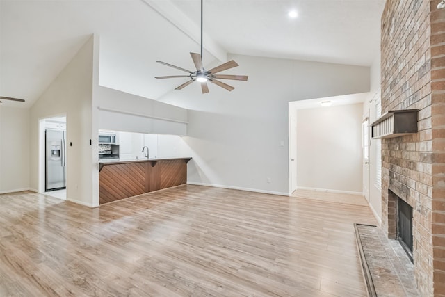 unfurnished living room featuring beam ceiling, sink, light hardwood / wood-style floors, and a brick fireplace