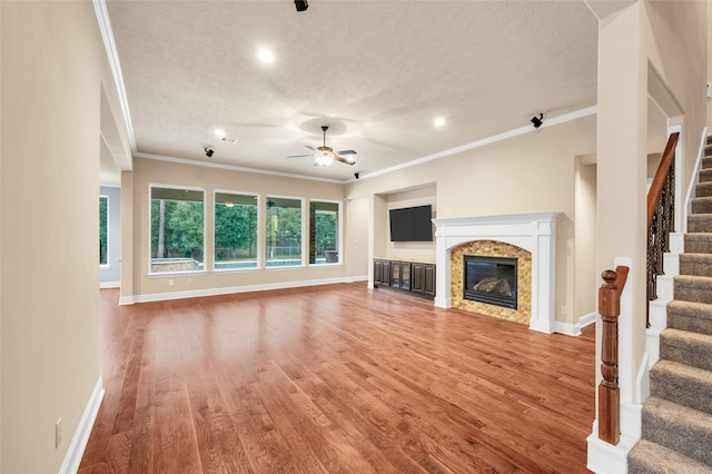 unfurnished living room featuring ceiling fan, crown molding, wood-type flooring, and a textured ceiling