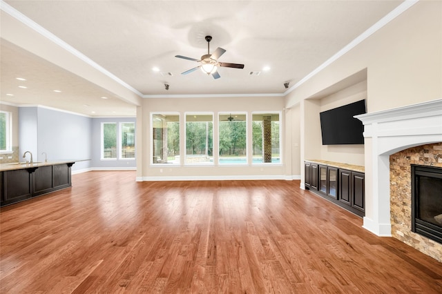 unfurnished living room with sink, ceiling fan, light wood-type flooring, ornamental molding, and a fireplace