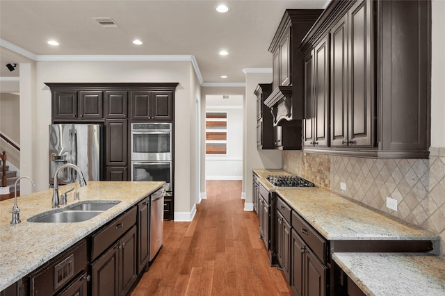 kitchen with light stone countertops, ornamental molding, dark brown cabinets, stainless steel appliances, and sink