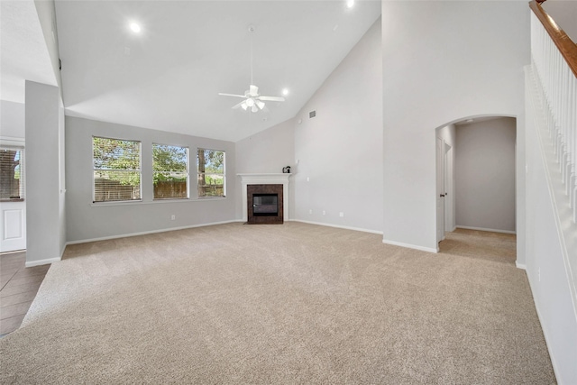 unfurnished living room featuring arched walkways, light colored carpet, ceiling fan, a fireplace with flush hearth, and high vaulted ceiling