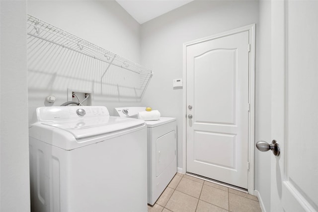 clothes washing area featuring laundry area, washing machine and dryer, light tile patterned floors, and baseboards