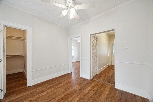 unfurnished bedroom featuring ceiling fan, a walk in closet, dark wood-type flooring, and a closet