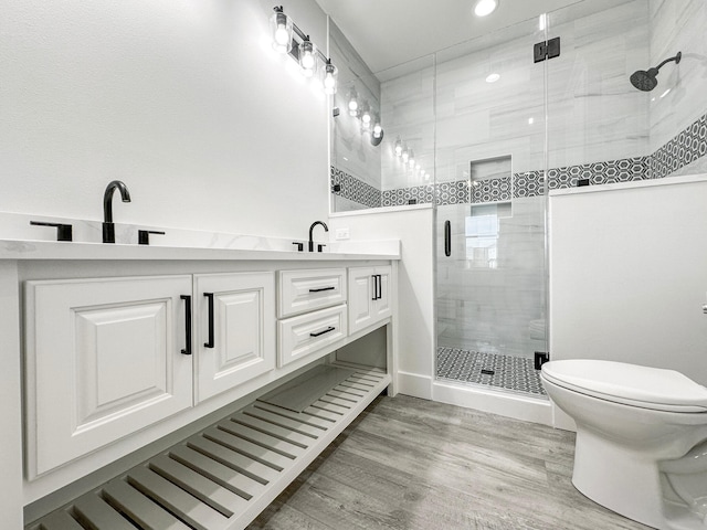 bathroom with hardwood / wood-style floors, vanity, a shower with shower door, and toilet