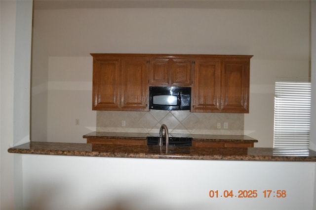 kitchen featuring black appliances, decorative backsplash, and dark stone countertops