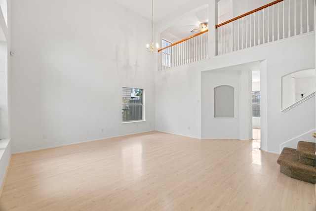 unfurnished living room featuring light wood-type flooring, a towering ceiling, and an inviting chandelier