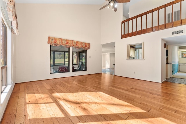 unfurnished living room with a wealth of natural light, ceiling fan, light hardwood / wood-style floors, and a high ceiling