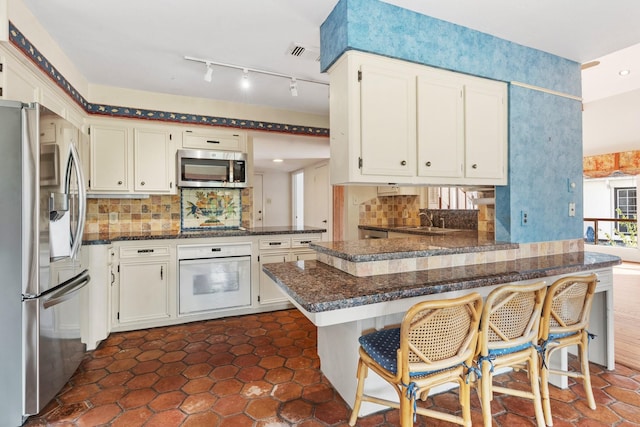 kitchen with kitchen peninsula, backsplash, stainless steel appliances, sink, and a breakfast bar area