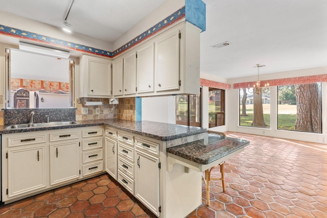 kitchen with sink, decorative backsplash, dark stone countertops, a kitchen bar, and kitchen peninsula