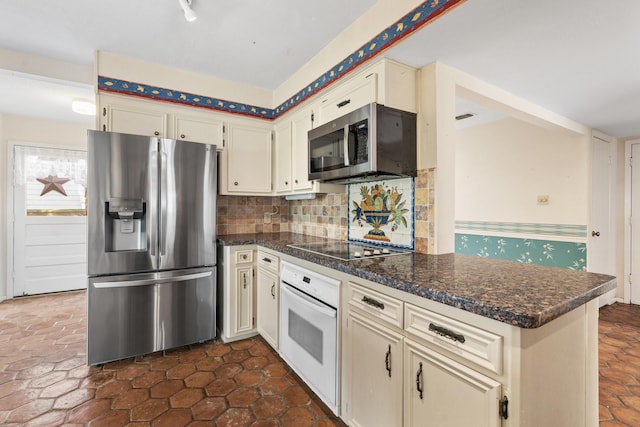 kitchen with backsplash, dark stone countertops, cream cabinetry, and appliances with stainless steel finishes