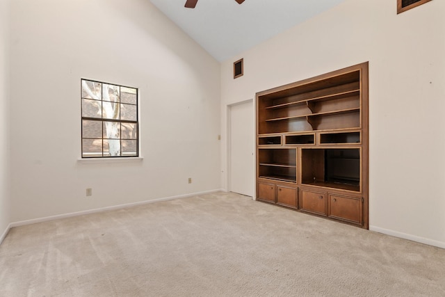 unfurnished living room with high vaulted ceiling, built in features, ceiling fan, and light colored carpet