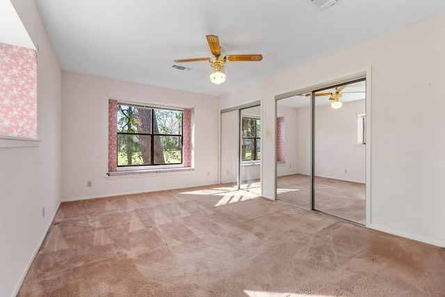 unfurnished bedroom with multiple closets, ceiling fan, and light colored carpet