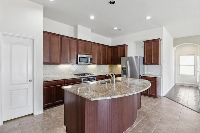 kitchen with a center island with sink, sink, light tile patterned floors, light stone counters, and stainless steel appliances