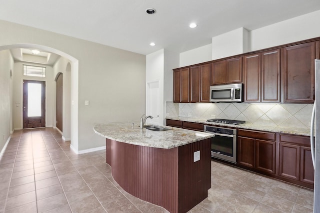 kitchen featuring sink, decorative backsplash, an island with sink, appliances with stainless steel finishes, and light stone counters