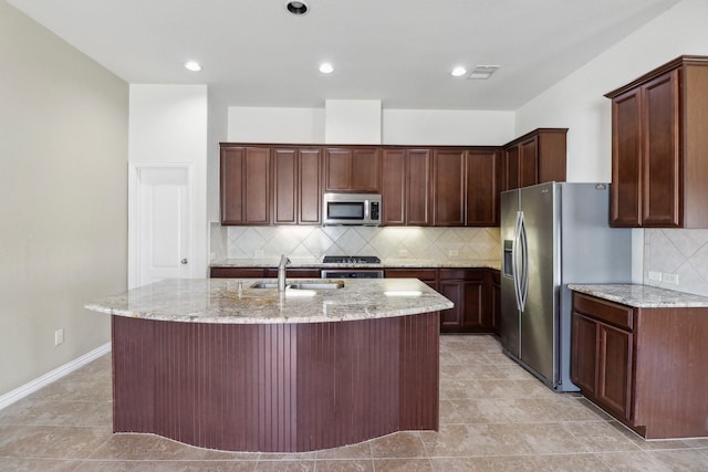 kitchen featuring sink, stainless steel appliances, light stone counters, backsplash, and a kitchen island with sink