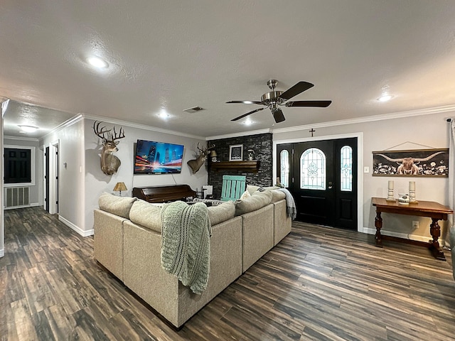 living room with a textured ceiling, a stone fireplace, dark wood-type flooring, and crown molding