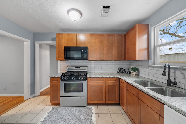 kitchen featuring sink, light stone counters, stainless steel gas stove, light tile patterned floors, and backsplash