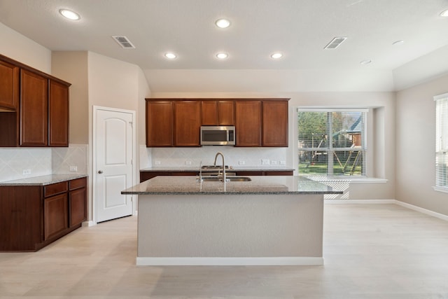 2206 Wolf Creek Ct, Katy, TX 77493 - kitchen featuring stainless steel microwave, a sink, dark stone countertops, recessed lighting, and a center island with sink