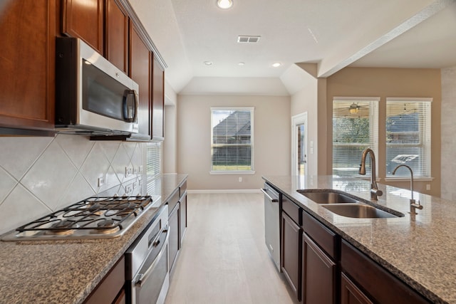 kitchen featuring backsplash, stone counters, sink, vaulted ceiling, and stainless steel appliances