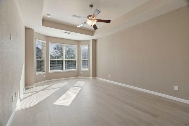 spare room with light hardwood / wood-style floors, a raised ceiling, and ceiling fan