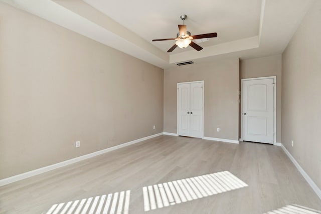 unfurnished bedroom featuring ceiling fan, a raised ceiling, and light hardwood / wood-style flooring