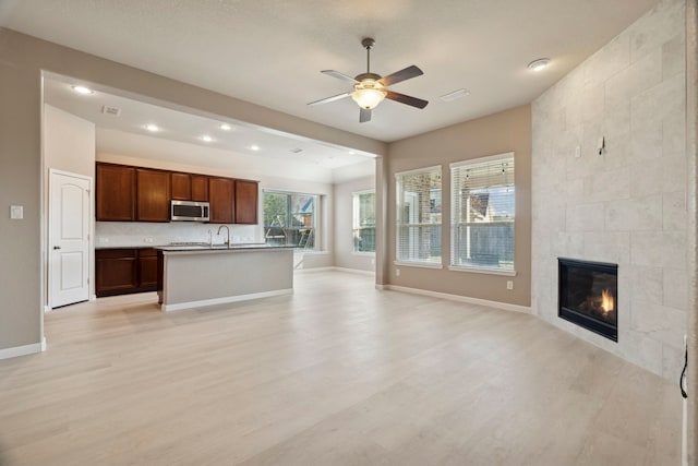 unfurnished living room featuring ceiling fan, a fireplace, and light hardwood / wood-style flooring