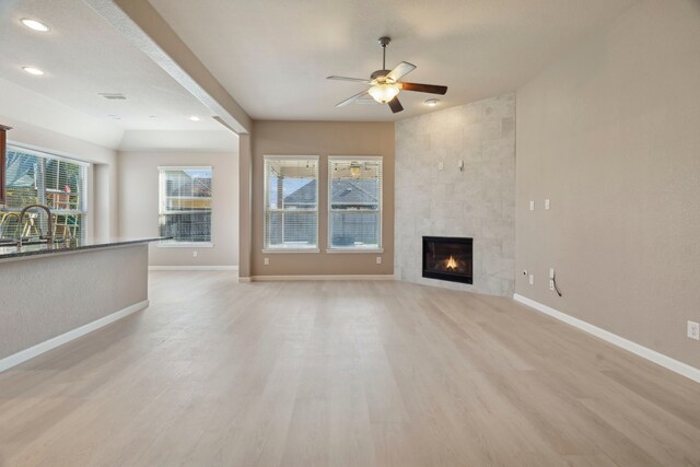 unfurnished living room featuring light wood-type flooring, ceiling fan, and a tiled fireplace