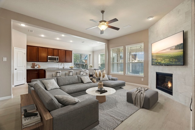 2206 Wolf Creek Ct, Katy, TX 77493 - living area featuring light wood-type flooring, baseboards, a ceiling fan, a tile fireplace, and recessed lighting