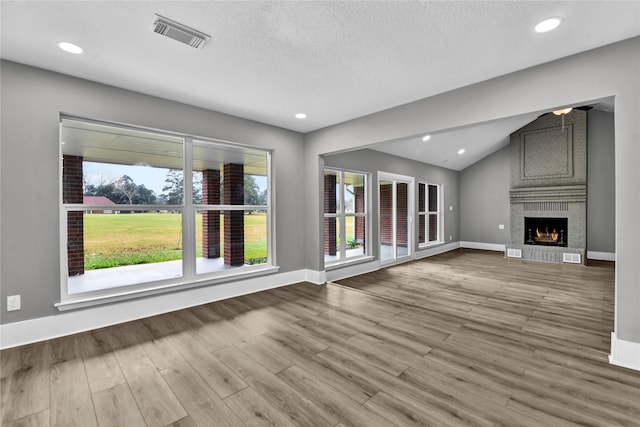 unfurnished living room with a textured ceiling, light hardwood / wood-style floors, a brick fireplace, and lofted ceiling