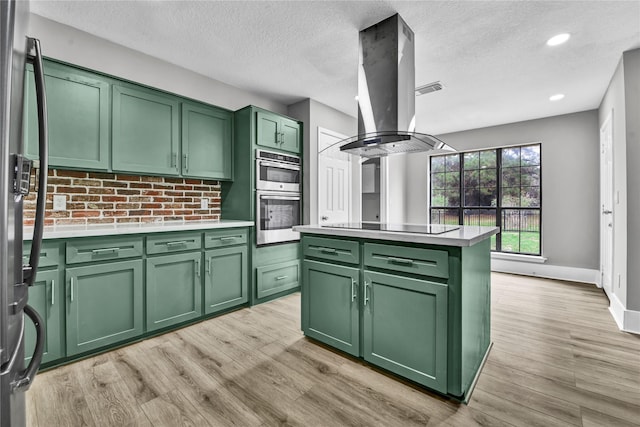 kitchen with green cabinetry, a kitchen island, appliances with stainless steel finishes, tasteful backsplash, and island range hood