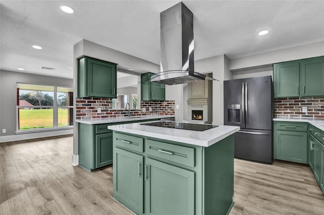 kitchen with a center island, green cabinets, stainless steel refrigerator with ice dispenser, black electric cooktop, and island exhaust hood