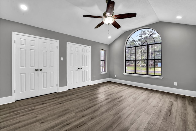 unfurnished bedroom featuring two closets, ceiling fan, dark wood-type flooring, and vaulted ceiling