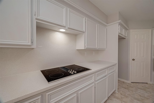 kitchen with black electric stovetop, light tile patterned flooring, and white cabinets