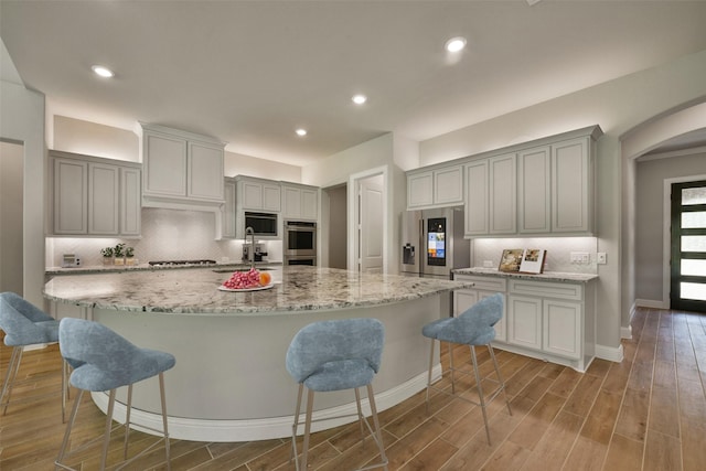 16146 Rustling Woods Rd, Conroe, TX 77302 - kitchen featuring appliances with stainless steel finishes, backsplash, wood finished floors, a breakfast bar area, and recessed lighting